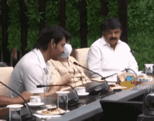 a man wearing a mask sits at a table with other people
