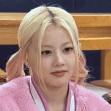a close up of a woman with blonde hair wearing a pink jacket and ponytail .