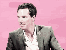 a man in a suit and white shirt is sitting in front of a pink background that says ellenemigo