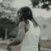 a man with dreadlocks is wearing a white tank top and is standing in front of a house .