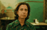 a woman in a green shirt is looking at the camera with a sad look on her face