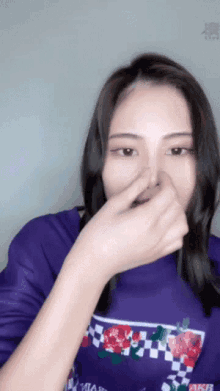 a woman wearing a purple shirt that says akb covers her nose