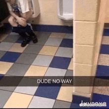 a man is squatting down in a public restroom next to a urinal with his pants down .