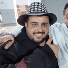 a man with a beard wearing a hat is giving a thumbs up while standing next to another man .