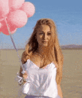a woman in a white tank top and purple skirt is holding pink balloons in the desert .