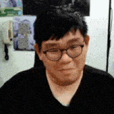 a man wearing glasses and a black shirt is smiling in front of a sign that says h.