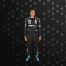 a man in a petronas racing suit stands in front of a black background