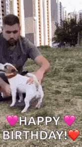 a man is petting a small dog in a field while a happy birthday message is displayed .