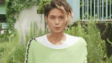 a young man wearing a green sweater and a white shirt is making a funny face
