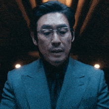 a man wearing glasses and a suit looks at the camera