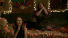 two women are sitting in a room with christmas lights and a fan in the background