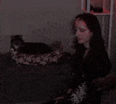 a woman sits next to a cat in a floral bed