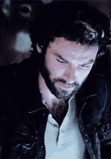 a man with a beard is wearing a black leather jacket