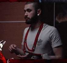 a man wearing a white shirt and a red necklace is flexing his arm