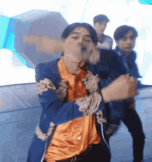 a man in a blue jacket and orange shirt is dancing .