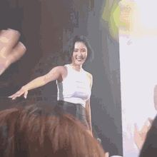a woman in a white tank top is standing on a stage in front of a crowd of people .