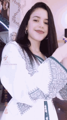 a young woman in a white dress with green embroidery is standing in front of a mannequin .