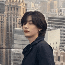a young man with his eyes closed stands in front of a cityscape