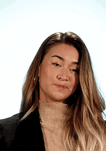 a woman with long blonde hair is wearing a black jacket and a gold top