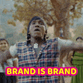 a man wearing a plaid shirt is standing in front of a sign that says brand is brand