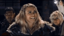 a woman in a black jacket is smiling in front of a crowd of people .