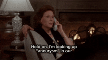 a woman sits in front of a fireplace talking on a cell phone and says hold on