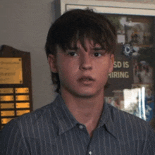 a young man in a striped shirt is standing in front of a bulletin board that says sd is hiring