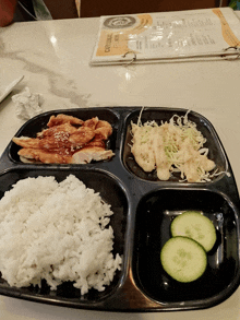 a tray of food with rice and cucumbers sits on a table in front of a menu