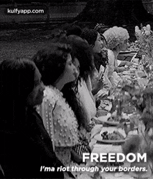 a black and white photo of a group of people sitting at a long table .
