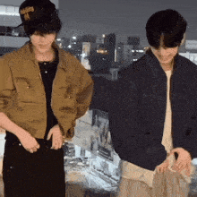 two young men are standing next to each other wearing jackets and hats . one of the hats has the letter m on it .