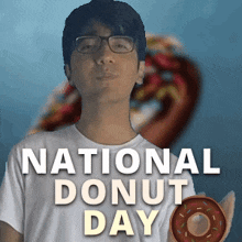 a man wearing glasses is holding a donut in front of a poster that says national donut day