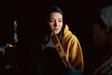 a woman in a yellow hoodie is holding a piece of paper in her hand and looking at it .