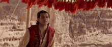 a man in a red vest is standing in front of a red tent in the desert .