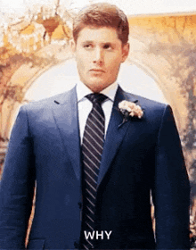 a man in a suit and tie is standing in front of a chandelier and looking at the camera .