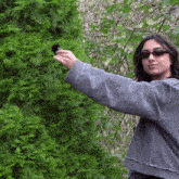 a woman wearing sunglasses is holding a black object in front of a tree