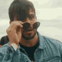 a man with a beard wearing sunglasses and a denim jacket .