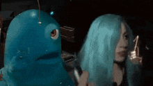 a woman with blue hair stands next to a blue monster