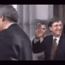 a man in a suit and tie is waving at another man in a suit and tie .