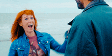 a man and a woman are standing on the beach and the man is wearing a blue jacket