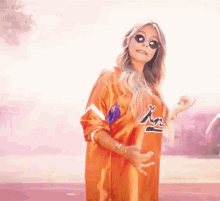 a woman wearing sunglasses and an orange jersey is standing in front of a pink car .