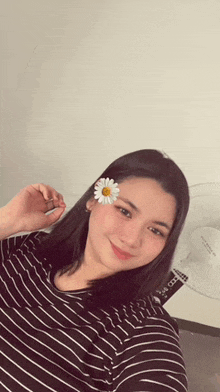a woman wearing a striped shirt with a flower in her hair is taking a selfie .