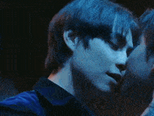 two men are kissing each other in a dark room with a blue background .
