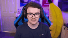 a man wearing glasses and headphones is sitting in a blue chair in front of a banana costume .