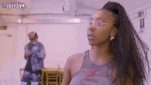 a woman wearing glasses and a tank top is standing in a room with a man in the background .