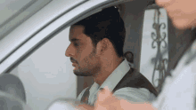 a man with a beard is sitting in a car talking to another man