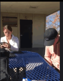 a man and a woman are sitting at a blue picnic table looking at their cell phones