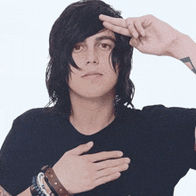 a young man wearing a black shirt and bracelets holds his hand to his chest