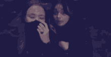 two women are sitting next to each other in a dark room and taking a selfie .