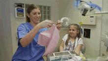 a woman in a blue scrub is helping a little girl with her dental exam
