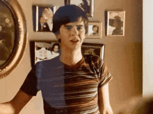 a young man in a striped shirt is standing in front of a mirror in a room .